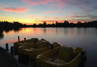 Solnedgang over en sø med gule pedalbåde ved Domaine d'Essendieras i Nouvelle-Aquitaine, Frankrig.