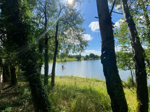 Sunny view through trees of a lake near Saint-Médard-d'Excideuil, Nouvelle-Aquitaine, France.