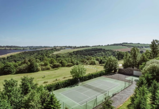 Scenic tennis court surrounded by lush greenery and rolling hills at Domaine d'Essendieras in France.