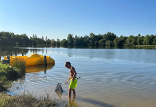 Junge fischt mit Kescher am See nahe Saint-Médard-d'Excideuil, Nouvelle-Aquitaine, Frankreich, bei Sonnenschein.