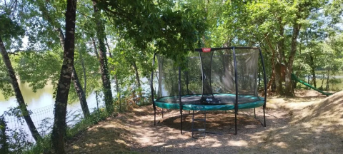 Trampoline in a shaded area near the lake at Domaine d'Essendieras holiday park, Nouvelle-Aquitaine, France.