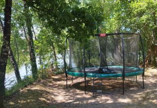 Trampoline in a shaded area near the lake at Domaine d'Essendieras holiday park, Nouvelle-Aquitaine, France.