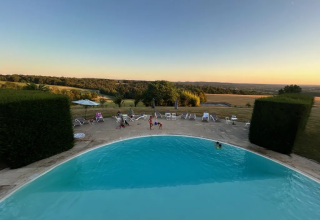 Vue sur la piscine et les transats au Domaine d'Essendieras, parc de vacances en Nouvelle-Aquitaine, France, au coucher du soleil.