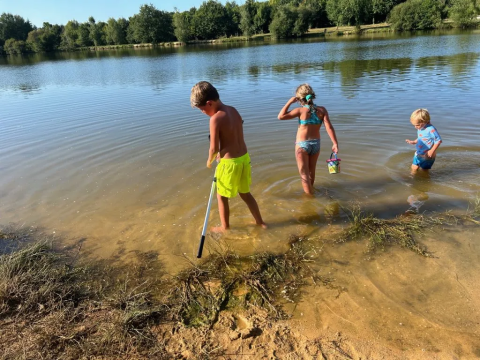 Tre bambini giocano nell’acqua bassa di un lago al Domaine d’Essendieras, parco vacanze in Nouvelle-Aquitaine, Francia.