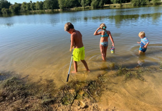 Drie kinderen spelen in het ondiep water aan een meer in Domaine d'Essendieras, vakantiepark in Nouvelle-Aquitaine, Frankrijk.