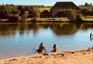 Twee personen zitten aan de oever van het meer bij Domaine d' Essendieras met huis en natuur op de achtergrond.