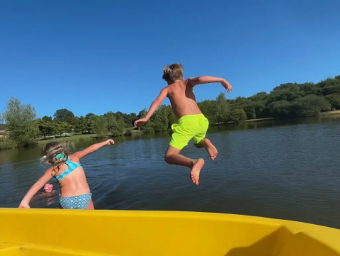 Niños saltan alegremente desde un barco amarillo al agua en Domaine d'Essendieras, Nouvelle-Aquitaine, Francia.