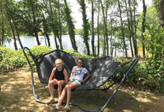 Twee kinderen zitten op een grote buitenhangmat bij het meer in Domaine d'Essendieras, Nouvelle-Aquitaine, Frankrijk.