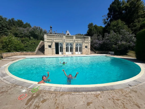 Kinderen zwemmen en spelen in een groot rond zwembad voor een elegant gebouw op Domaine d' Essendieras.