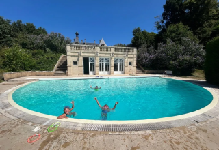 Børn leger i en stor, rund swimmingpool foran en elegant bygning på Domaine d' Essendieras i Frankrig.