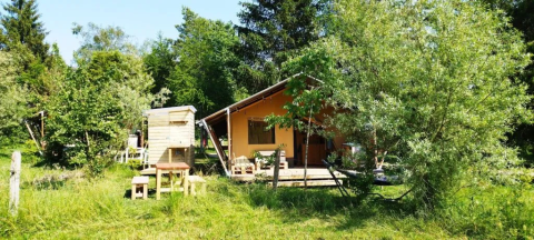 Photo of a safari tent with bathroom surrounded by trees and greenery in a peaceful nature setting.