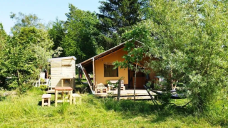 Photo of a safari tent with bathroom surrounded by trees and greenery in a peaceful nature setting.