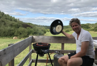 Homme faisant griller des saucisses sur terrasse avec vue sur la vallée à Safaritent met badkamer, Domaine d'Essendieras.