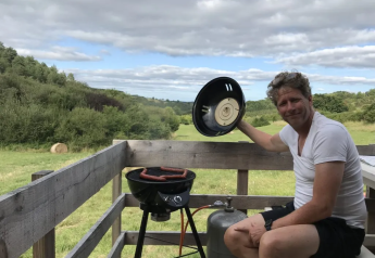 Man grilling sausages on a terrace with valley views at Safaritent met badkamer, Domaine d'Essendieras, France.