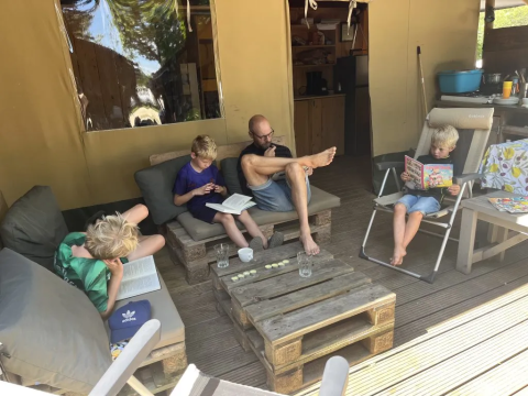Family reading and relaxing outside a safari tent with bathroom at Domaine d'Essendieras in France.