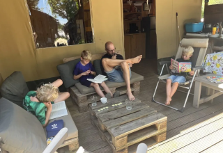 Family reading and relaxing outside a safari tent with bathroom at Domaine d'Essendieras in France.