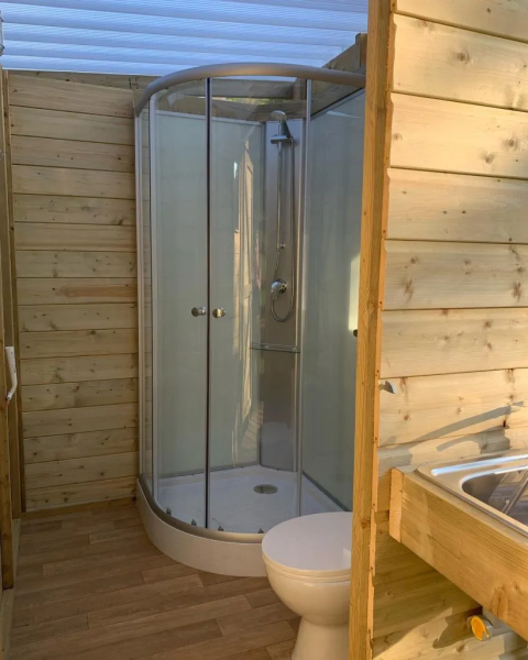 Salle de bain moderne avec murs en bois, douche, toilettes et lavabo dans une tente safari à Domaine d'Essendieras.