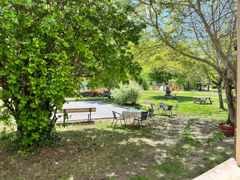 Vista soleggiata su un campeggio in Occitania, Francia, con tavoli, sedie, alberi e area giochi per bambini.