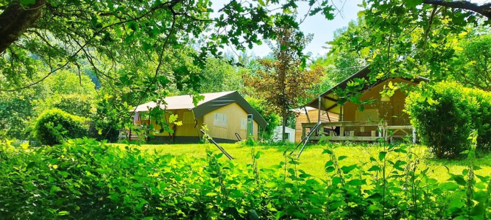 Safaritent met badkamer op camping La Prade in Frankrijk, omgeven door groene natuur en bomen.