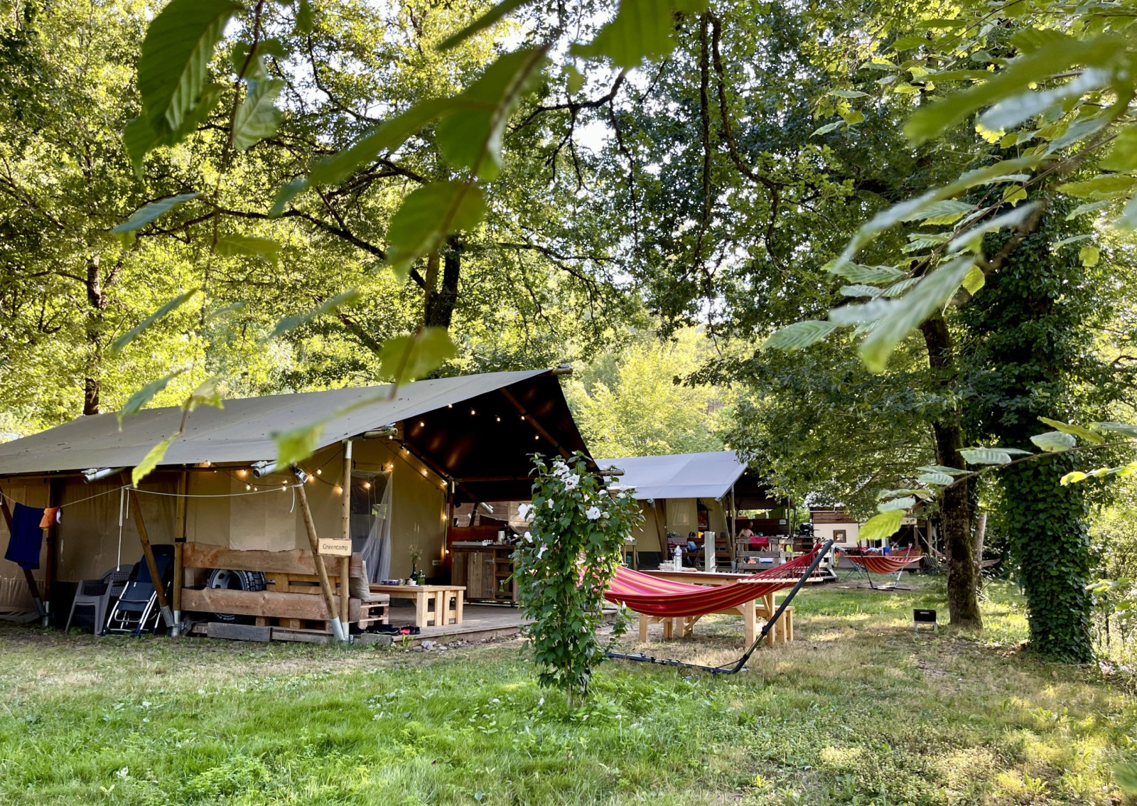 Safaritent met badkamer op Camping La Prade in Frankrijk, omgeven door bomen, groen en hangmatten.