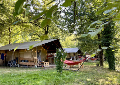 Safaritent met badkamer op Camping La Prade in Frankrijk, omgeven door bomen, groen en hangmatten.