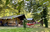 Tenda safari con bagno al campeggio La Prade in Francia, circondata da alberi e amache colorate.