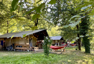 Safaritent met badkamer op Camping La Prade in Frankrijk, omgeven door bomen, groen en hangmatten.