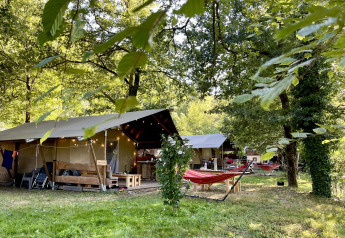 Tenda safari con bagno al campeggio La Prade in Francia, circondata da alberi e amache colorate.