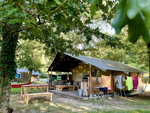 Safaritent met badkamer op Camping La Prade in Frankrijk, omgeven door bomen en kampeerfaciliteiten.
