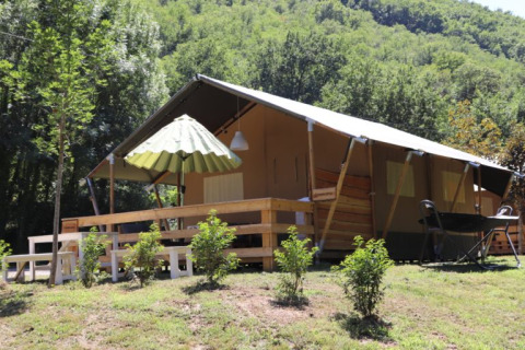 Tenda safari con bagno al campeggio La Prade in Francia, circondata da colline verdi e alberi fitti.