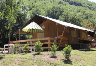Tenda safari con bagno al campeggio La Prade in Francia, circondata da colline verdi e alberi fitti.