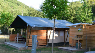 Tenda safari con bagno esterno, angolo cottura e terrazza in legno, circondata dalla natura verde.