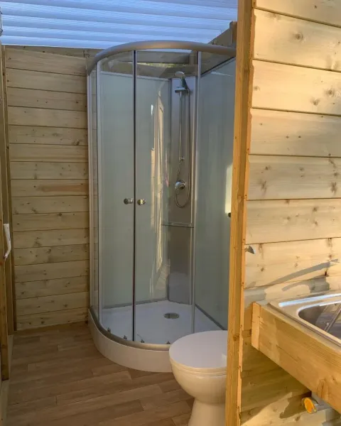 Bathroom in a safari tent with a glass shower, toilet, wooden walls and natural daylight streaming in.
