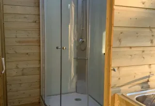 Bathroom in a safari tent with a glass shower, toilet, wooden walls and natural daylight streaming in.