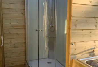 Badeværelse i et safaritelt med brusekabine, toilet og trævægge, oplyst af naturligt lys.