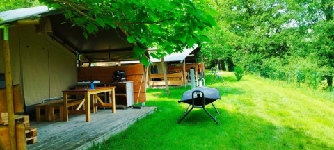 Tenda safari con bagno presso il campeggio La Prade in Francia, con tavolo, barbecue e prato verde.
