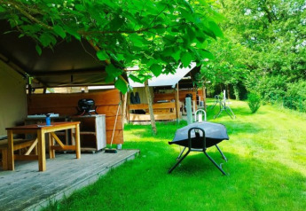 Tenda safari con bagno presso il campeggio La Prade in Francia, con tavolo, barbecue e prato verde.