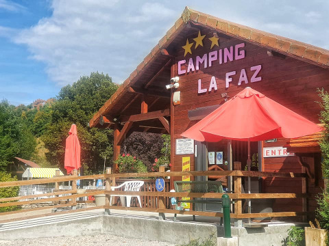 Ingresso al campeggio La Faz in Bourgogne-Franche-Comté, Francia, con edificio in legno e ombrelloni rossi.