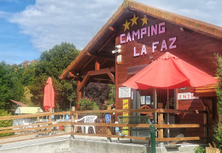 Ingresso al campeggio La Faz in Bourgogne-Franche-Comté, Francia, con edificio in legno e ombrelloni rossi.