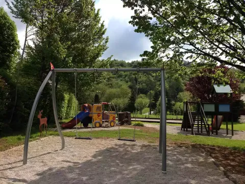 Parco giochi al campeggio La Faz con altalene e scivolo, circondato da alberi in Borgogna, Francia.