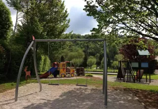 Parco giochi al campeggio La Faz con altalene e scivolo, circondato da alberi in Borgogna, Francia.