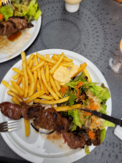 Un piatto con patatine fritte, insalata e spiedino di carne servito su un tavolo al campeggio La Faz, Francia.