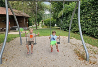 Due bambini seduti sulle altalene in un campeggio a Bourgogne-Franche-Comté, Francia, circondati dal verde.