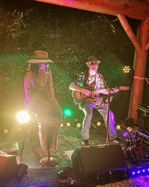 Due musicisti si esibiscono su un palco all'aperto al Campsite La Faz in Bourgogne-Franche-Comté, Francia, di notte.