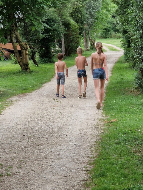 Tre bambini in costume da bagno camminano su un sentiero ghiaioso al campeggio La Faz, Bourgogne-Franche-Comté, Francia.