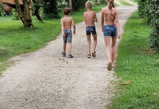 Tre bambini in costume da bagno camminano su un sentiero ghiaioso al campeggio La Faz, Bourgogne-Franche-Comté, Francia.