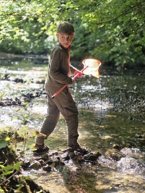 Ragazzo con un retino in un ruscello al Campeggio La Faz, Bourgogne-Franche-Comté, Francia, immerso nella natura.