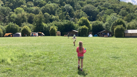 Bambini che giocano su un prato al campeggio La Faz, con tende e baite, immersi nel verde della Francia.