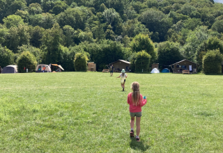 Bambini che giocano su un prato al campeggio La Faz, con tende e baite, immersi nel verde della Francia.