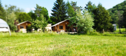 Safari tent with bathroom at Campsite La Faz in France, set among green trees and a grassy meadow.